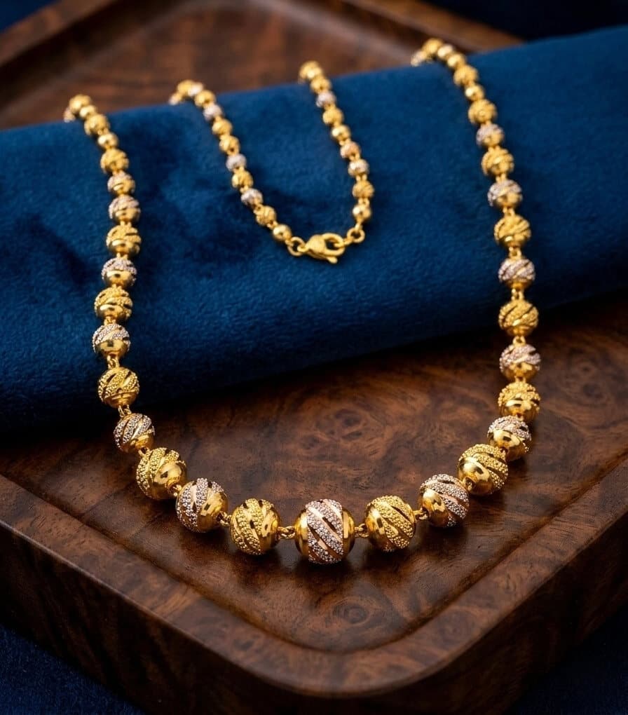 A 22ct gold ball-bead chain with two-tone patterned beads, on a wooden tray