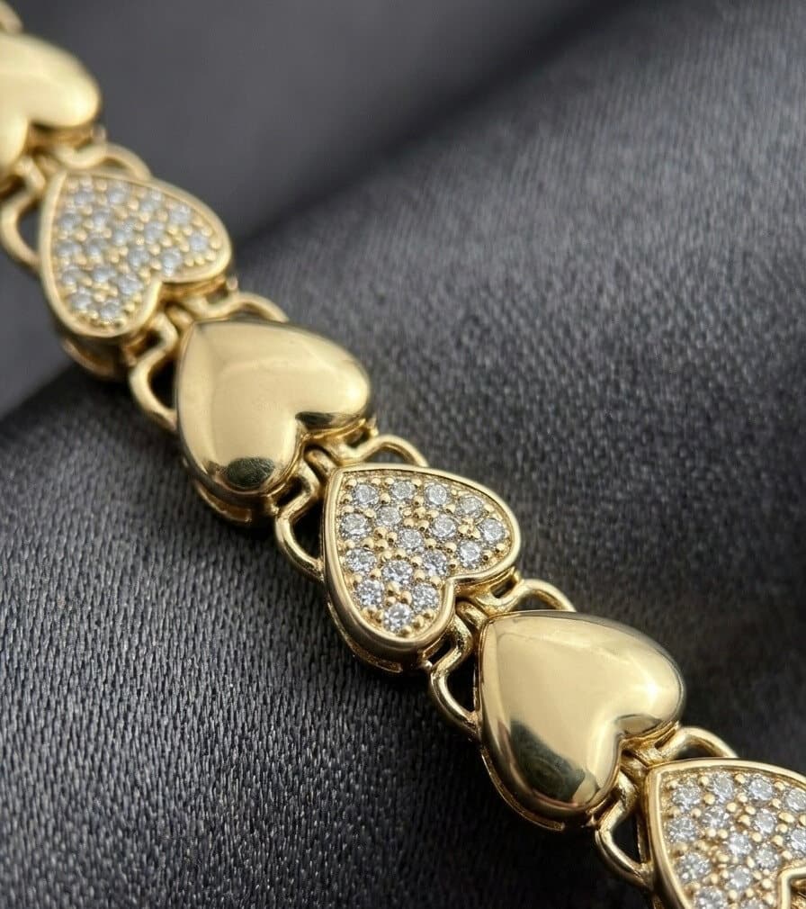 Close-up of a gold bracelet of alternating polished and stone-set hearts