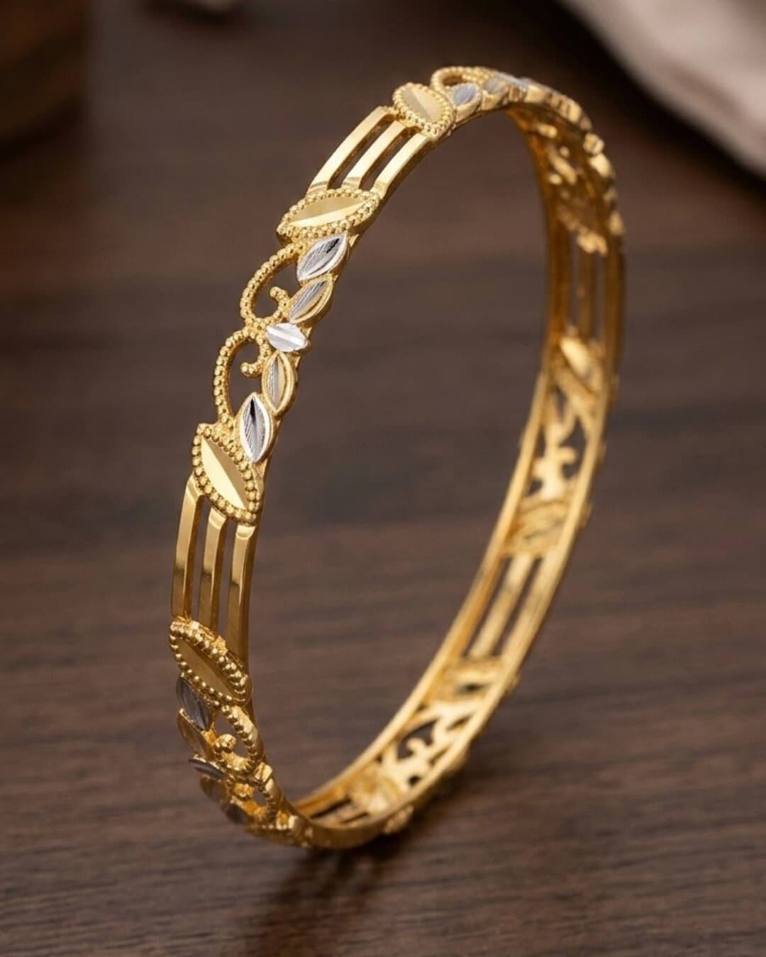 A 22ct gold openwork bangle with two-tone leaf detail, on dark wood
